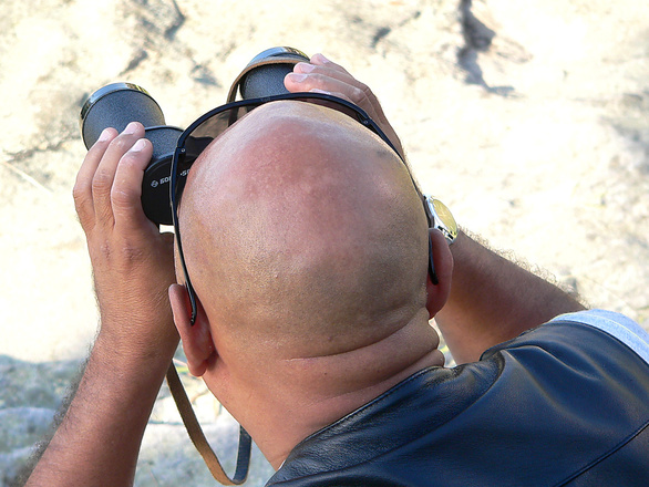 man with binoculars looking for ways to regrow hair on a bald head